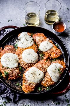 chicken parmesan in a cast iron skillet with two glasses of wine on the side