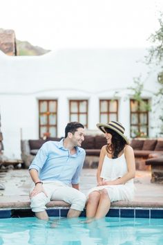 a man and woman sitting on the edge of a swimming pool