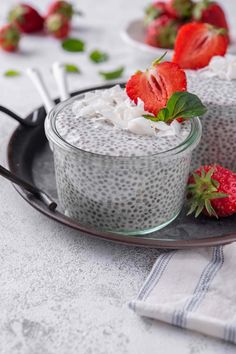 two desserts with strawberries and whipped cream on a black serving platter next to spoons