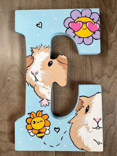 the letter j is painted with pictures of hamsters and flowers on blue wood background