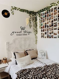 a white bed topped with lots of pillows next to a wall covered in pictures and plants