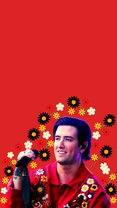 a man holding a microphone in front of a red background with daisies and flowers