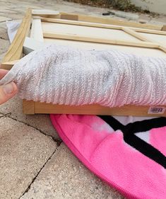 someone is holding something in their hand near a pink surfboard that has been placed on the ground