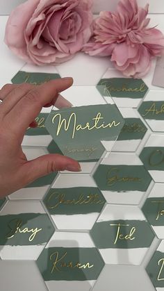 a person's hand on top of a table with place cards and flowers in the background