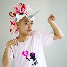 a young man wearing a pink shirt with scissors on it's head and holding his fist up