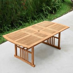 a wooden table sitting on top of a cement floor next to green grass and bushes