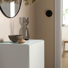 a vase with some flowers in it sitting on a white cabinet next to a mirror