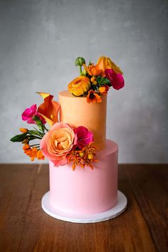 a three tiered cake decorated with flowers on top of a wooden table next to a gray wall