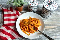 a white plate topped with pasta next to two potted plants on top of a wooden table