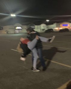 two people are hugging in an empty parking lot at night with the lights turned on