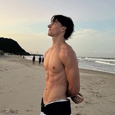 a man standing on top of a sandy beach next to the ocean in swim trunks