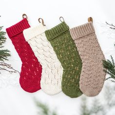 four knitted stockings hanging from hooks on a white surface with evergreen branches and snow