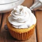 a cupcake with white frosting sitting on top of a wooden table next to a bowl