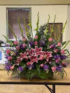 a large arrangement of flowers on a table in a room with wooden floors and windows