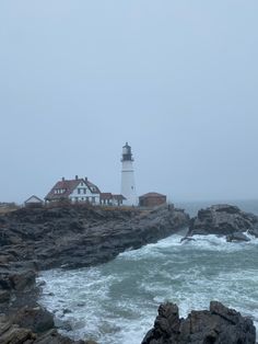 a light house sitting on top of a rocky cliff next to the ocean with waves crashing in front of it