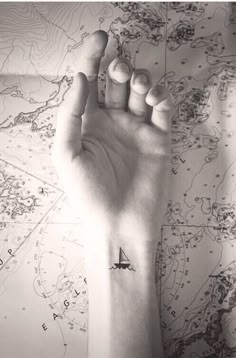 a person's hand with a small sailboat tattoo on the middle of their arm