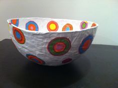 a paper bowl sitting on top of a table next to a white wall with circles painted on it