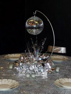 the table is set with silver plates and silver balls on top of each plate,