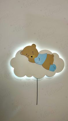 a teddy bear sleeping on top of a cloud shaped night light that is lit up