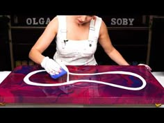 a woman in white aprons waxing a piece of art with purple and red paint