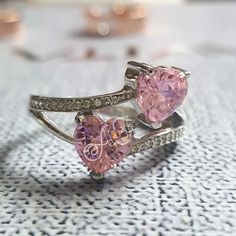 two heart shaped pink diamond rings sitting on top of a white cloth covered tablecloth