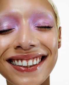 a close up of a person smiling with pink eyeshadow on her face and white teeth