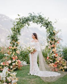 a woman wearing a wedding dress standing in front of an archway with flowers and greenery