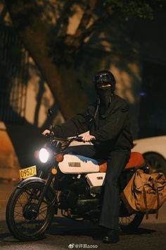 a man riding on the back of a white motorcycle down a street next to a tree