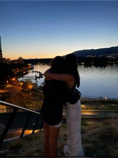 two people embracing each other in front of a body of water at sunset or dusk