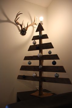 a christmas tree made out of wooden planks with ornaments on the top and antlers mounted to the wall