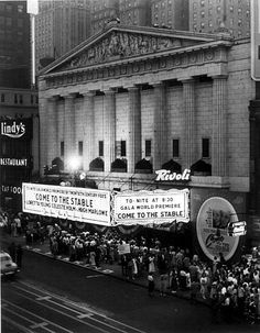 an old black and white photo of people standing in front of a building with large billboards