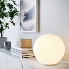 a white lamp sitting on top of a table next to a potted plant and books