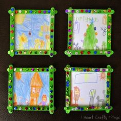 four children's artwork pieces are displayed in green frames on a brown table top