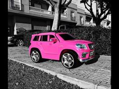 a pink suv parked on the side of a road next to a tree and bushes