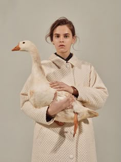 a woman is holding a duck in her arms while standing against a gray background,