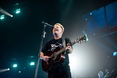 a man singing into a microphone while holding a guitar in front of him on stage