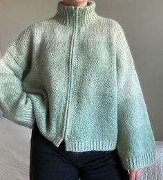 a woman standing in front of a bed wearing a green sweater