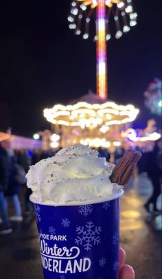 someone holding up a cup of ice cream in front of a carnival ride