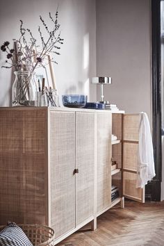 a wooden cabinet with glass vases on top of it next to a lamp and other items