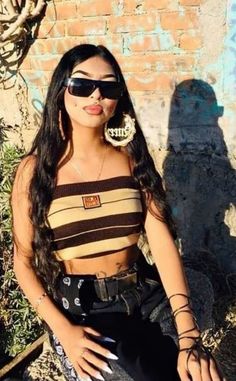 a woman sitting on the ground wearing black and tan clothing with sunglasses, holding her hand up to her chest