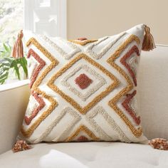 a decorative pillow with tassels sits on a couch in front of a window