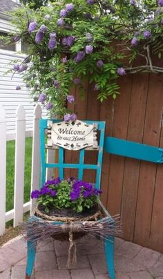 a blue chair sitting on top of a brick patio next to a fence with purple flowers growing in it