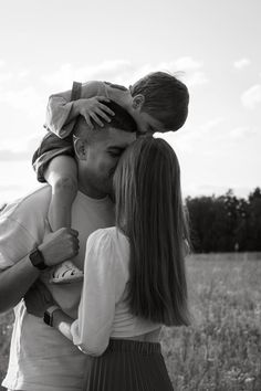 a black and white photo of a man kissing a woman's forehead while holding a small child