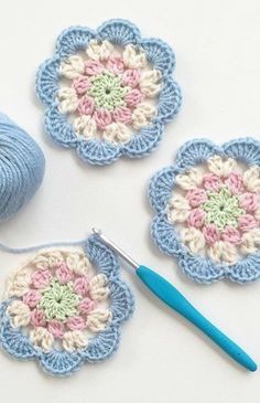 three crocheted flowers are next to a ball of yarn and a knitting needle