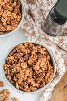 two bowls filled with walnuts next to a bottle of water on a white surface