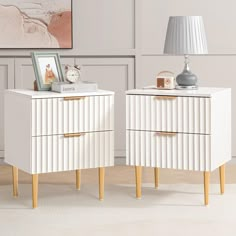 two white nightstands sitting next to each other in front of a painting on the wall