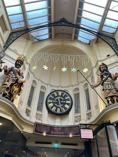 the clock is hanging from the ceiling in the building's atrium area, with statues and lights on either side