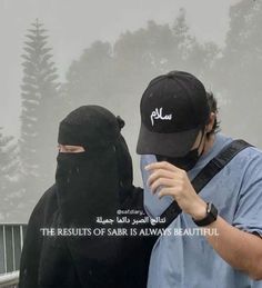 two people wearing burkas are standing in front of a foggy forest and one is looking at his cell phone