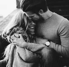 a man and woman hugging each other while sitting on the ground with their arms around each other