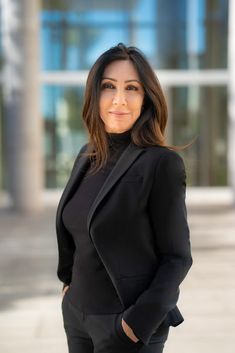 a woman standing in front of a building wearing a black suit and heels with her hands on her hips